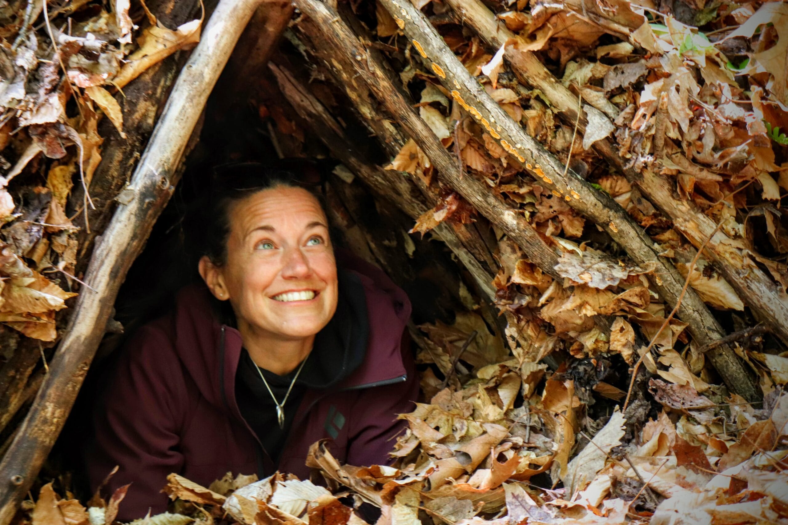 student crawling into a leaf-insulated debris shelter