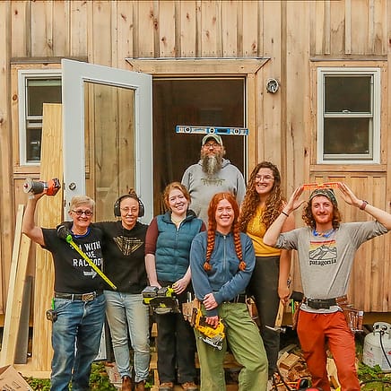 smiling students standing in front of the tiny house they worked to build and finish out as a donation from Wild Abundance carpentry school to a victim of Hurricane Helene who lost housing.