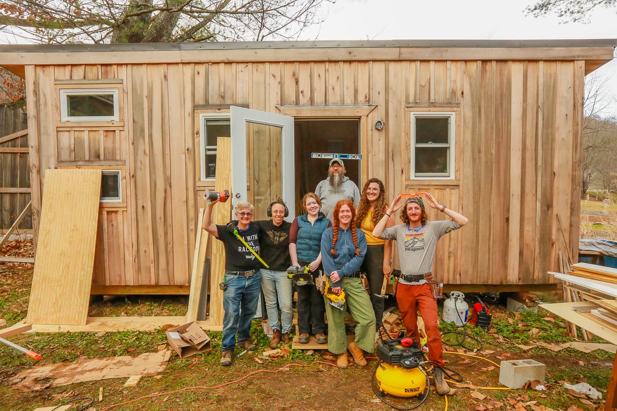 About us 4 month carpentry training program-1200-Current-622 Students in a 4 month carpentry training program smile for a group picture with the tiny home they built and finished from scratch to donate to a victim of Hurricane Helene who lost housing and is in need.