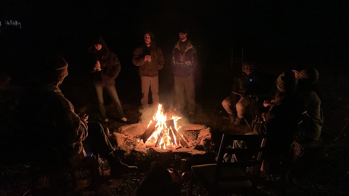 Students hanging out around a firepit at night at Wild Abundance